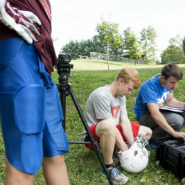 Virginia Tech doctoral students Ryan Gellner, center, and Eamon Campolettano, right, check the sensors in each youth player's helmet before every practice. The sensors measure head acceleration, helping the researchers determine when the players sustain the most severe impacts.