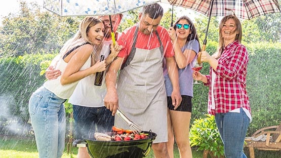 Man grilling food outside in the rain with umbrella