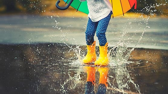 child playing in rain puddle with umbrella and boots