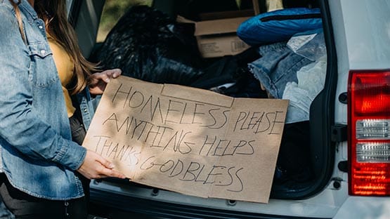 Woman holding homeless god bless sign in front of van