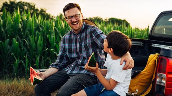 farmer and son eating watermelon in corn field