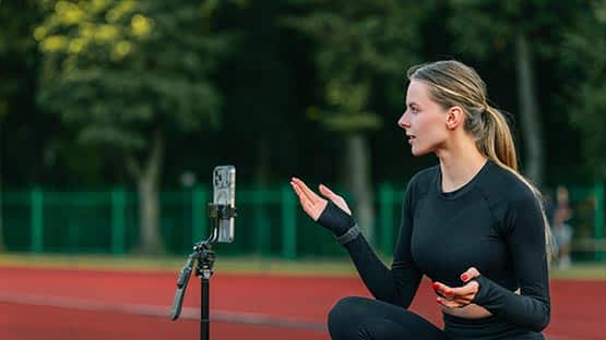 Fitness influencer recording workout tutorial on smartphone at outdoor track